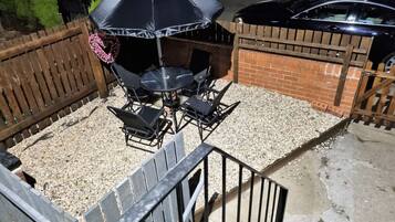 A patio area with a grill, outdoor seating, and a gravel surface.