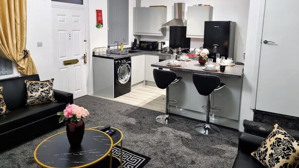 A modern kitchen with a central island, a dining area with two bar stools, a sofa set, and a washing machine. - *11BR* Setup for your most amazing relaxed stay + Free Parking + Free Fast WiFi (West Yorkshire)