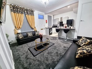 A modern living room with a black sofa, a round coffee table, and a black and gold patterned rug.