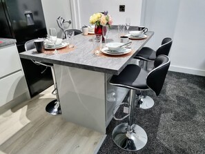 A modern kitchen with a central island, bar stools, and a dining table set for four.