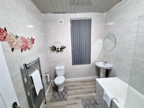 A bathroom with a toilet, sink, and bathtub, tiled walls, and a window with curtains.