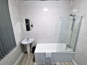 Une salle de bain avec une douche à parois de verre, un lavabo sur colonne et un miroir.