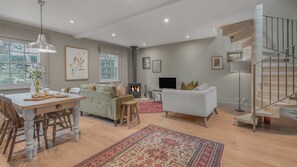 A spacious living area with a fireplace, a dining table, and a staircase. - Claytons Retreat - Cotswold Country Escape (Lower Oddington)