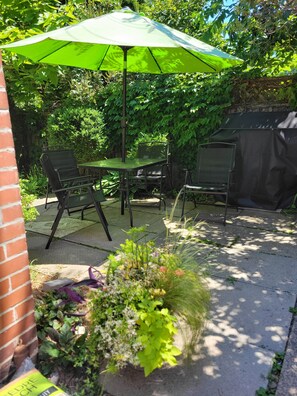 A patio with a green umbrella, metal chairs, a table, and a garden area with plants. - Victorian on Herkimer (Hamilton)