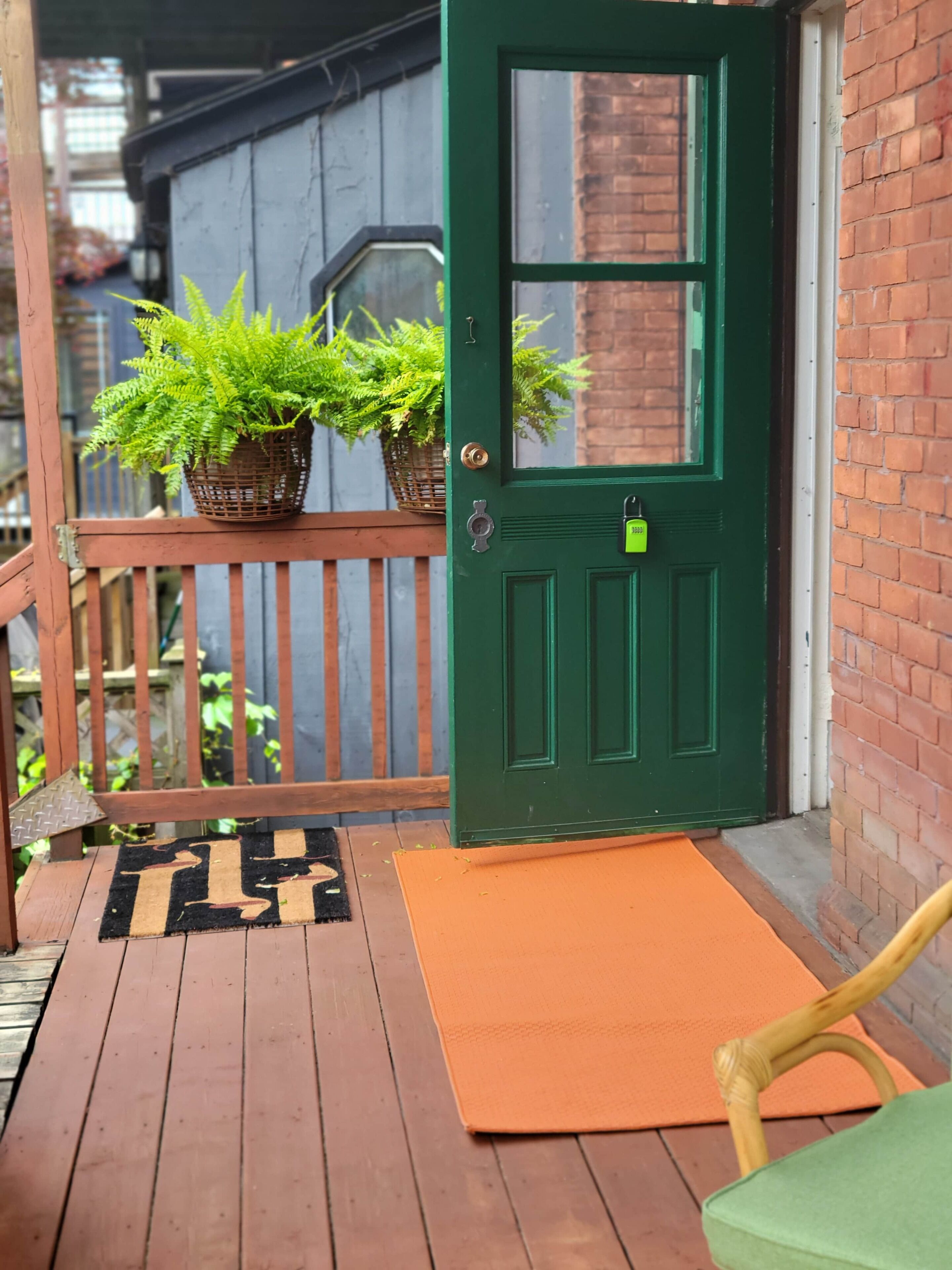 Una porta verde con una finestra, un molo in legno, un cesto di vimini con piante e un tappetino d'ingresso.