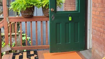 Una porta verde con una finestra, un molo in legno, un cesto di vimini con piante e un tappetino d'ingresso.