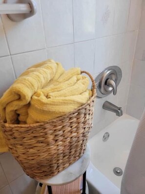 A bathroom with a white tiled wall, a wicker basket with yellow towels, and a bathtub.