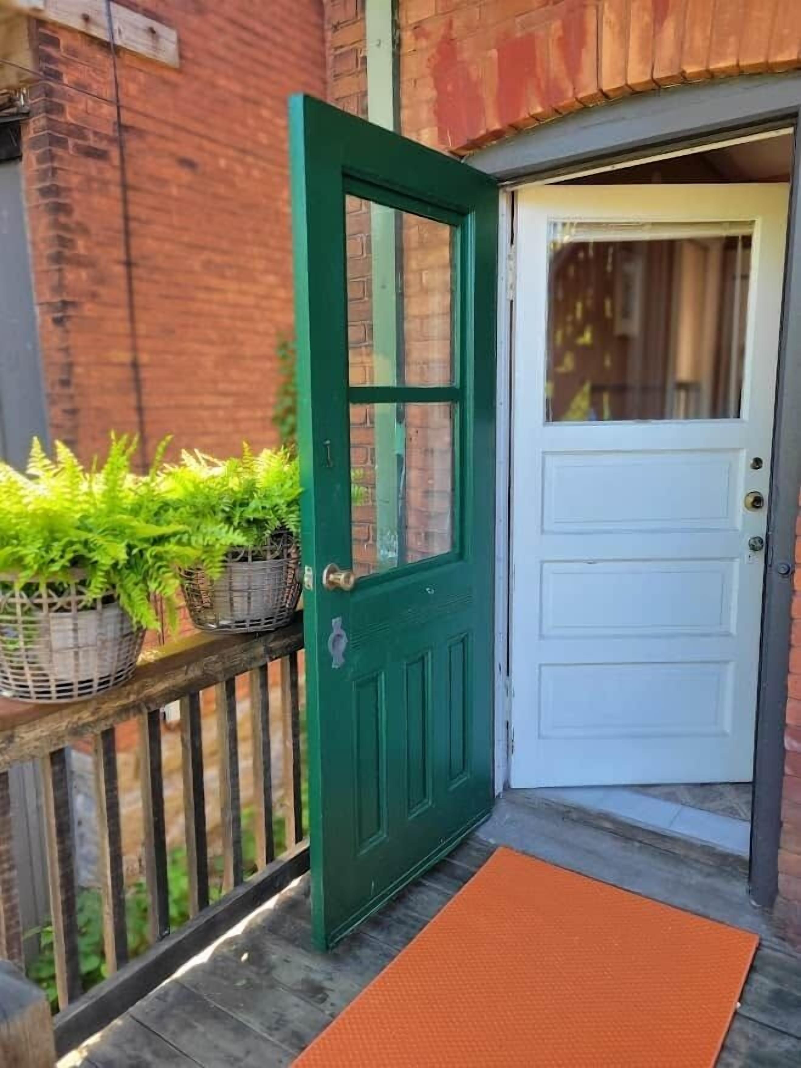 A green door with a white door beside it, a wooden fence, and potted plants on the fence.