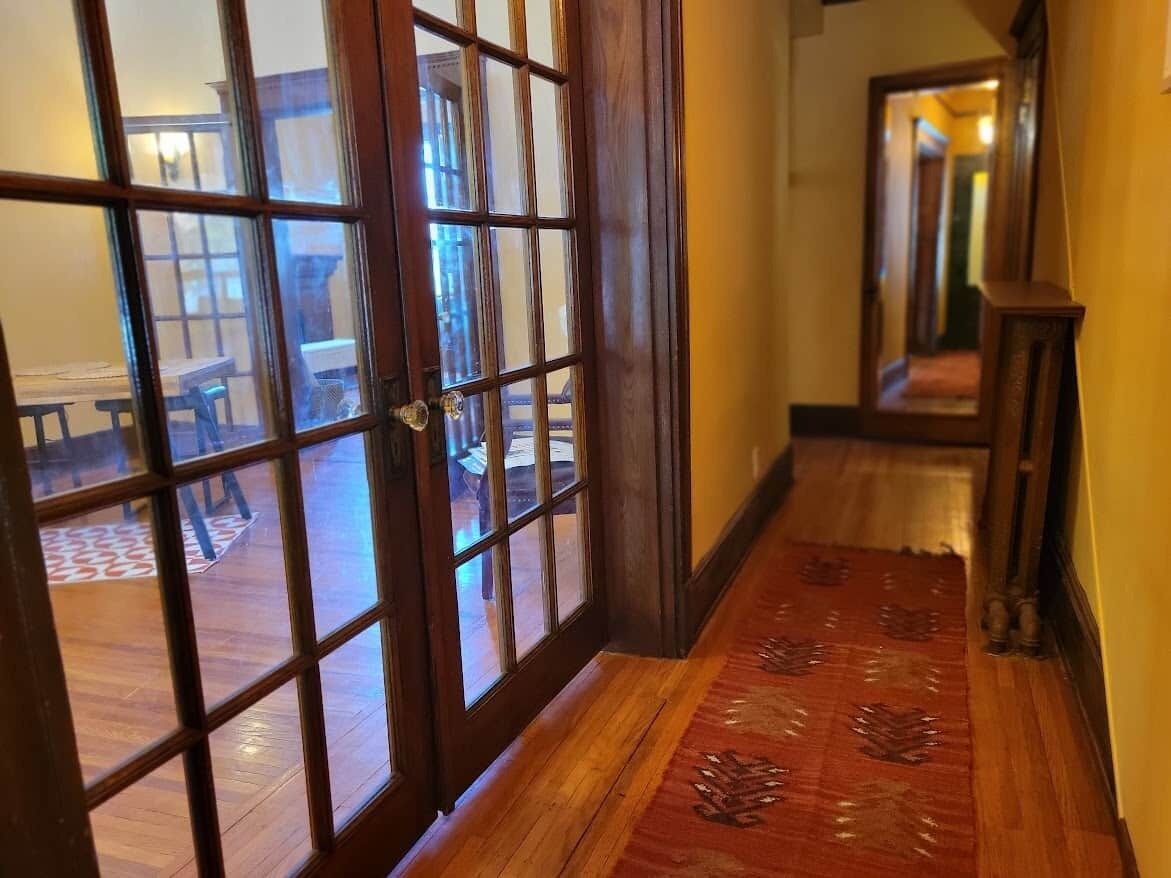 A wooden door with glass panels, a patterned carpet, and a hallway leading to a room with a table and chairs.