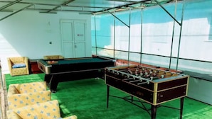Habitación con mesa de fútbol, alfombra verde y sillas estampadas de color amarillo.