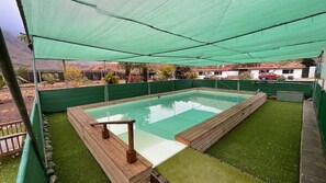 Ein Schwimmbecken mit Holzterrasse und einer grünen Netz-Markise.