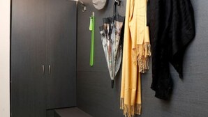 Une chambre moderne avec une armoire gris foncé, un banc et un porte-manteau mural sur lequel sont accrochés un foulard jaune et une veste noire.