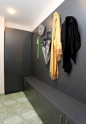 Ein modernes Zimmer mit einem dunkelgrauen Kleiderschrank, einer Bank und einem an der Wand befestigten Kleiderhaken mit gelbem Schal und schwarzer Jacke.