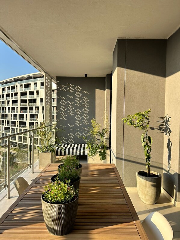 A balcony with a wooden floor, potted plants, and a view of a building. - Explore Ellipse (Midrand)
