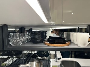 A kitchen area with a shelf holding various dishes and glasses. - Explore Ellipse (Midrand)