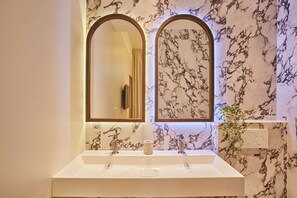 Ein Badezimmer mit einem weißen Waschbecken, zwei Spiegeln und Wänden mit Marmoroptik.