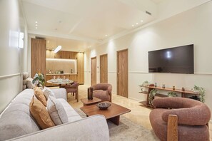 Ein modernes Wohnzimmer mit einer Couch, Sesseln, einem Couchtisch, einem Fernseher und einem Essbereich.