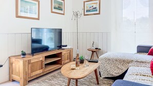 Una camera moderna con una TV a schermo piatto su un supporto in legno, un tavolino con una bottiglia e dei bicchieri, una statua di Buddha e un letto con biancheria a motivi.