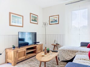 Ein modernes Zimmer mit einem Flachbildfernseher auf einem Holzboden, einem kleinen Tisch mit einer Flasche und Gläsern, einer Buddha-Statue und einem Bett mit gemusterten Betttextilien.