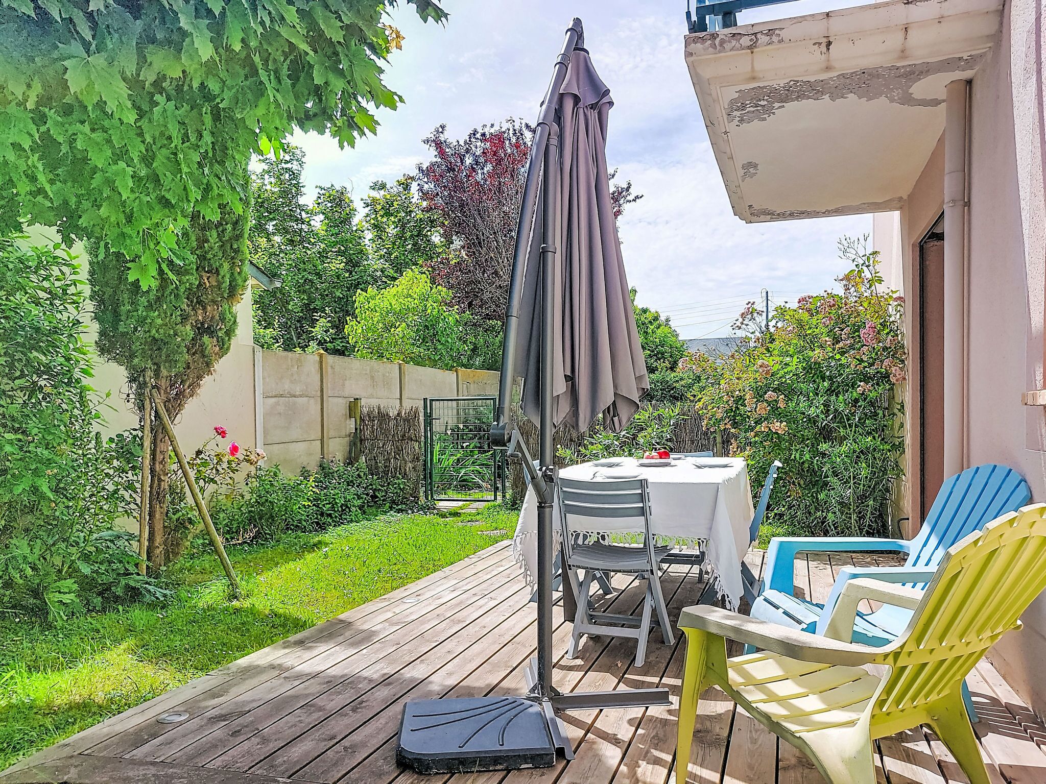 Una terraza de madera con una mesa y sillas, rodeada de follaje y un jardín.