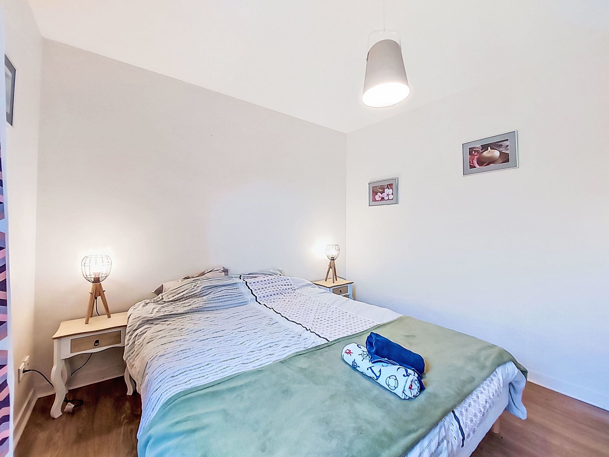 Quarto com cama, duas mesas de cabeceira, luminária pendente e dois quadros na parede.