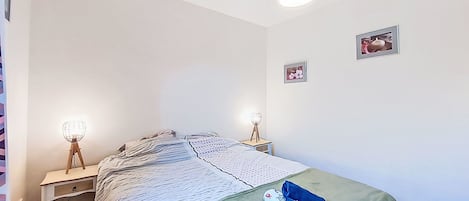 Une chambre à coucher comprenant un lit, deux tables de chevet, un luminaire suspendu et deux tableaux accrochés au mur.