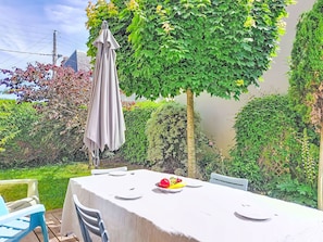 An outdoor dining area with a table set for two, surrounded by lush greenery and a pergola. - Claudel by Interhome (Saint Malo)