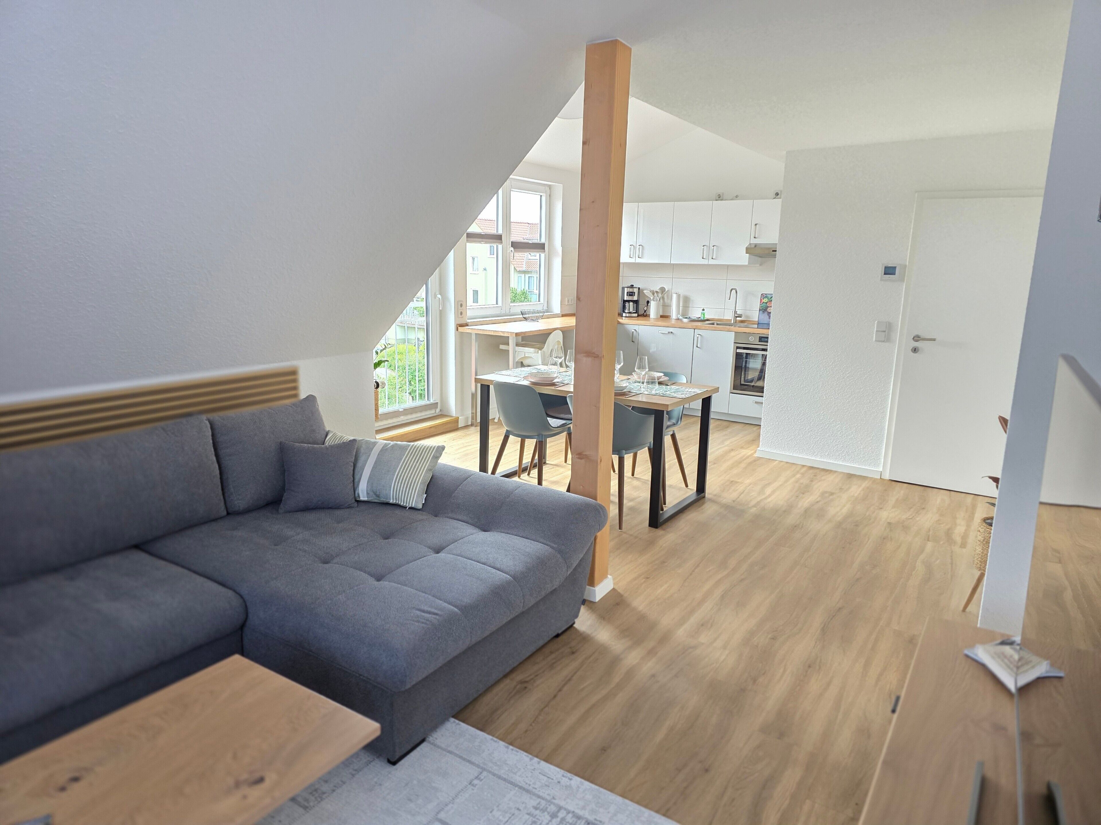 Una sala de estar moderna con un sofá seccional gris, una mesa de comedor de madera con sillas, y una cocina al fondo.