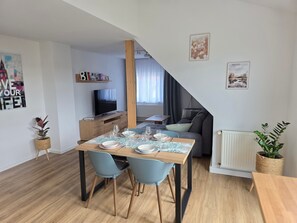 A modern living space with a dining area, a sofa, a TV, and a staircase. - Apartment Rückerts Gartenblick with Shared Garden (Nordhausen)