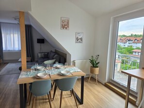 A dining area with a table set for four, a sofa, a radiator, a plant, and a view of buildings through a window. - Apartment Rückerts Gartenblick with Shared Garden (Nordhausen)