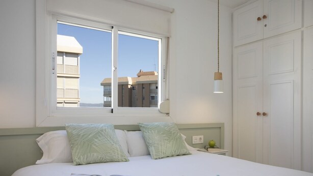A bedroom with a bed, pillows, a window, a nightstand, and a wardrobe. - Immerse yourself in the ultimate summer experience in this exclusive designer retreat, created for those seeking tranquility infused with Mediterranean charm. This apartment stands out for its bright and contemporary interior design, where every detail h (La Pobla de Farnals)
