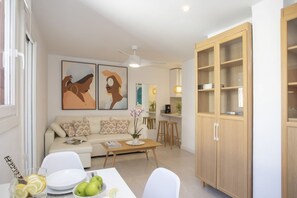 Ein Wohnzimmer mit einer Couch, einem Couchtisch und Kunstwerken. Es gibt eine Küchenzeile mit Hockern und einem Schrank.