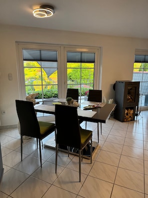 A dining area with a table and chairs, a fireplace, and a view of a garden through large windows.
