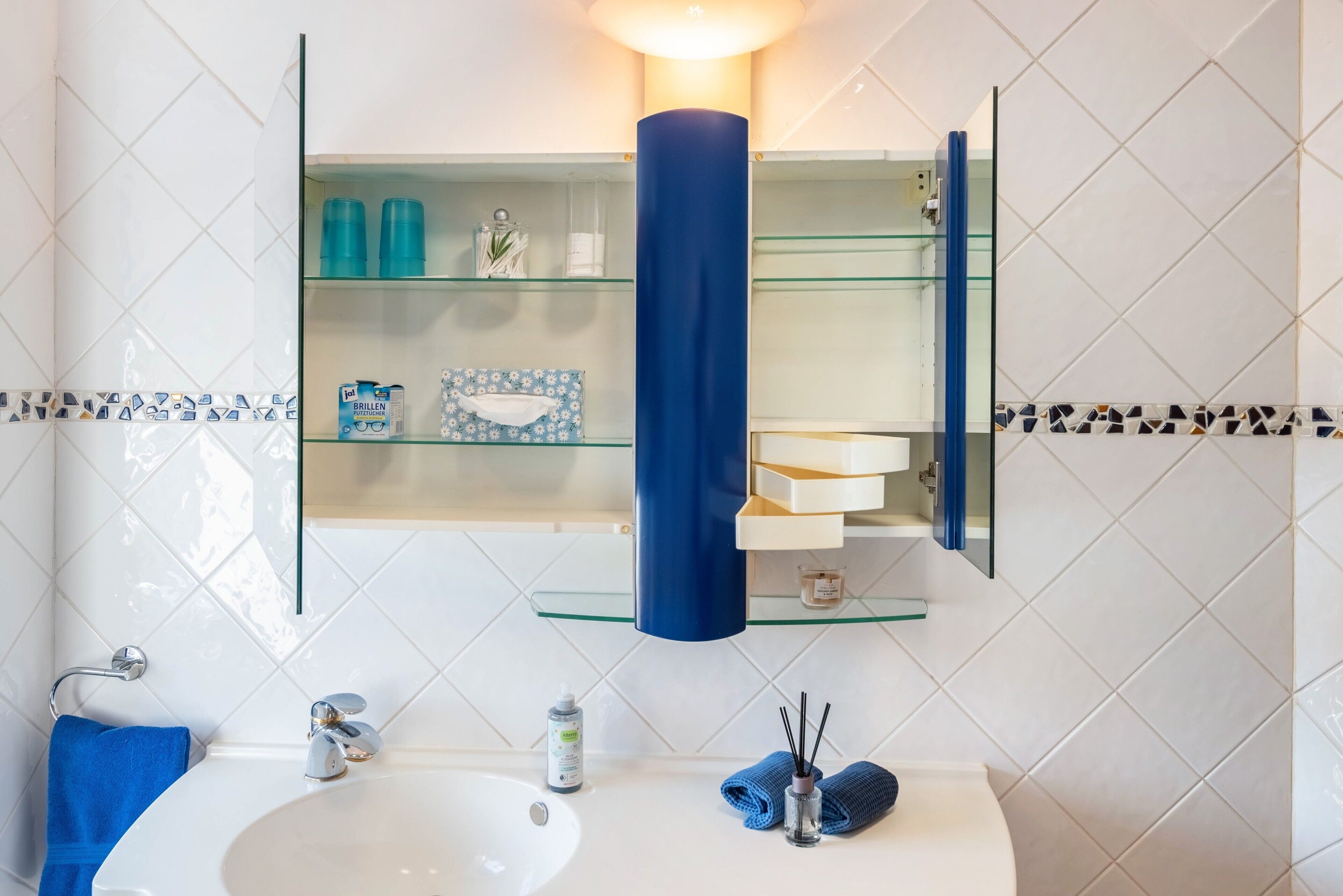 Ein Badezimmer mit einem weißen Waschbecken, einem blauen Handtuch und einer Glasablage für Pflegeprodukte.