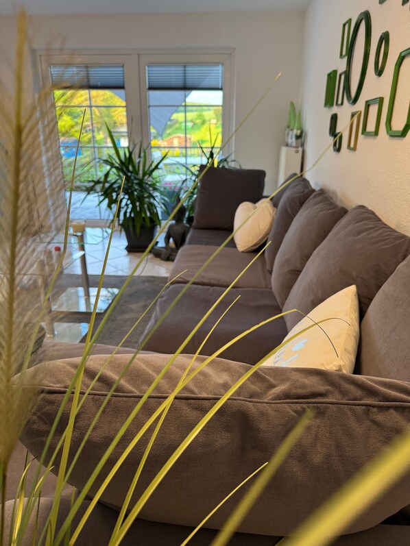 A living room with a brown sofa, a potted plant, and a window with blinds.
