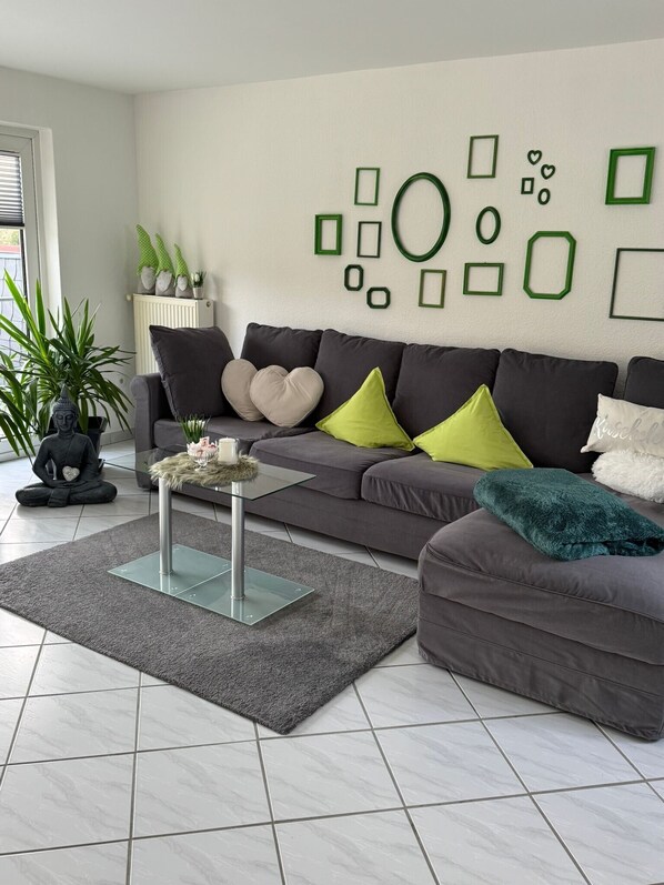 A modern living room with a grey sofa, a glass coffee table, and a grey rug.