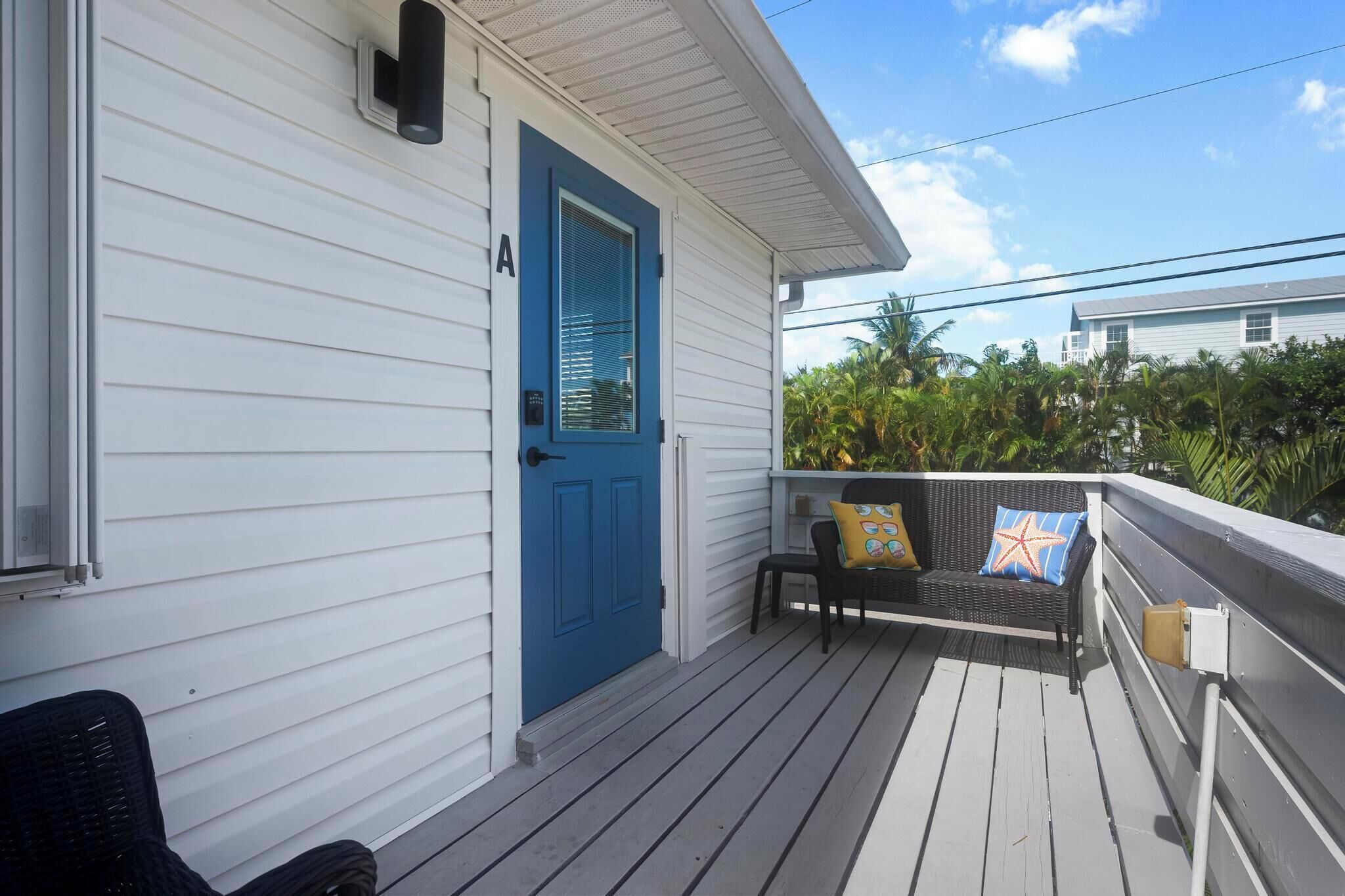 A porch with a blue door, a black wicker chair, and a bench with colorful cushions.