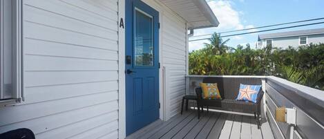 A porch with a blue door, a black wicker chair, and a bench with colorful cushions.