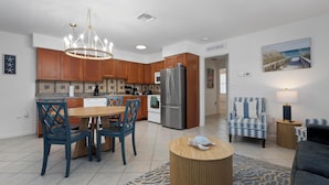 A modern kitchen with wooden cabinets, a stainless steel refrigerator, and a dining area with blue chairs. - Fantastic 1-bedroom home, short walk to beach. (Holmes Beach)