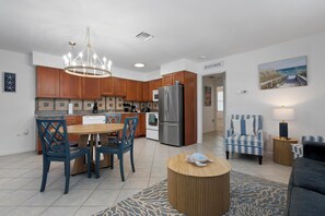 A modern kitchen with wooden cabinets, a stainless steel refrigerator, and a dining area with blue chairs. - Anna Maria Island - Newly renovated. Short walk to the beach. New Hot tub. (Holmes Beach)