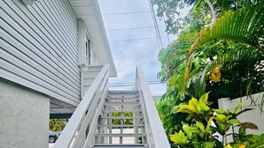 A white staircase leading up to a house with a white exterior and a lush green garden. - Fantastic 1-bedroom home, short walk to beach. (Holmes Beach)