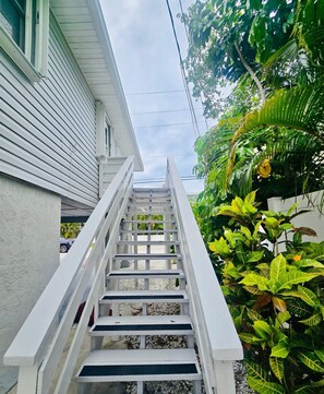 Eine weiße Treppe führt zu einem Haus mit weißer Fassade und einem üppigen, grünen Garten.