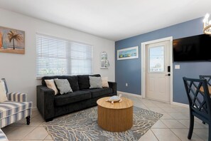 A living room with a dark-colored sofa, a striped armchair, a round wooden coffee table, and a patterned rug. - Anna Maria Island - Newly renovated. Short walk to the beach. New Hot tub. (Holmes Beach)