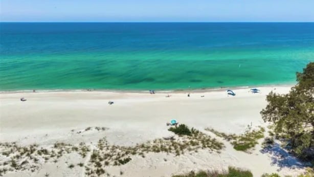 A beach with clear turquoise water, sandy shore, and sparse vegetation. - Fantastic 1-bedroom home, short walk to beach. (Holmes Beach)