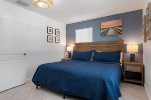 A bedroom with a bed, nightstands, a lamp, a picture on the wall, and a door. - Anna Maria Island - Newly renovated. Short walk to the beach. New Hot tub. (Holmes Beach)