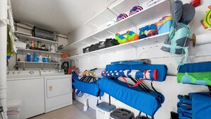 A laundry room with a washing machine, dryer, shelves with cleaning supplies, and various bags and equipment. - Anna Maria Island - Newly renovated. Short walk to the beach. New Hot tub. (Holmes Beach)
