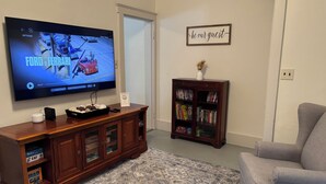 Una sala de estar con televisor de pantalla plana, una estantería, un sillón gris y una alfombra estampada.