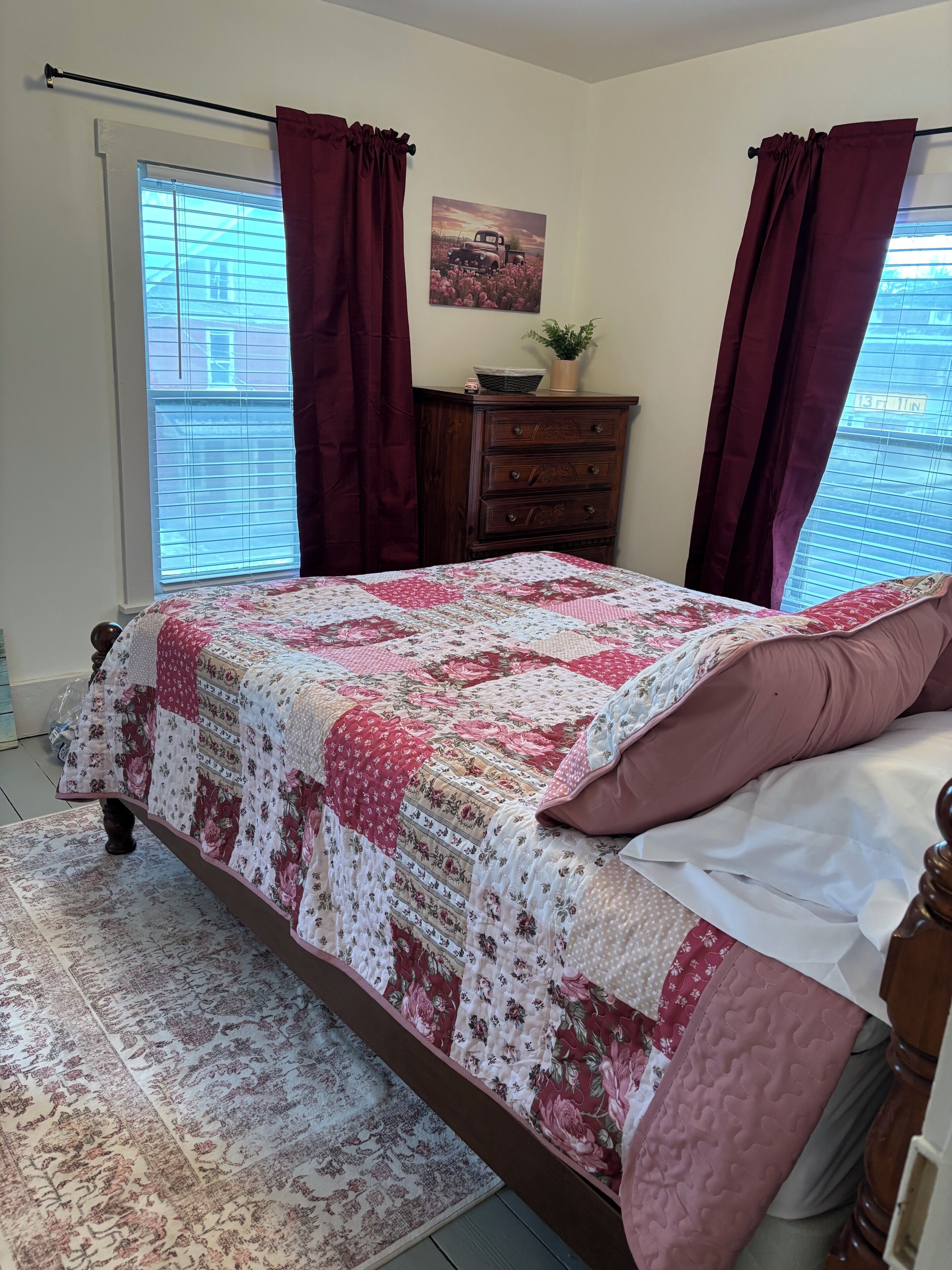 A bedroom with a bed, a dresser, a window with curtains, and a painting on the wall.