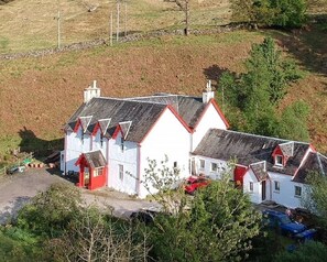 A cluster of white buildings with red accents, a gravel driveway, and a parked car. - Single room-Economy-Ensuite-Mountain view (Crianlarich)