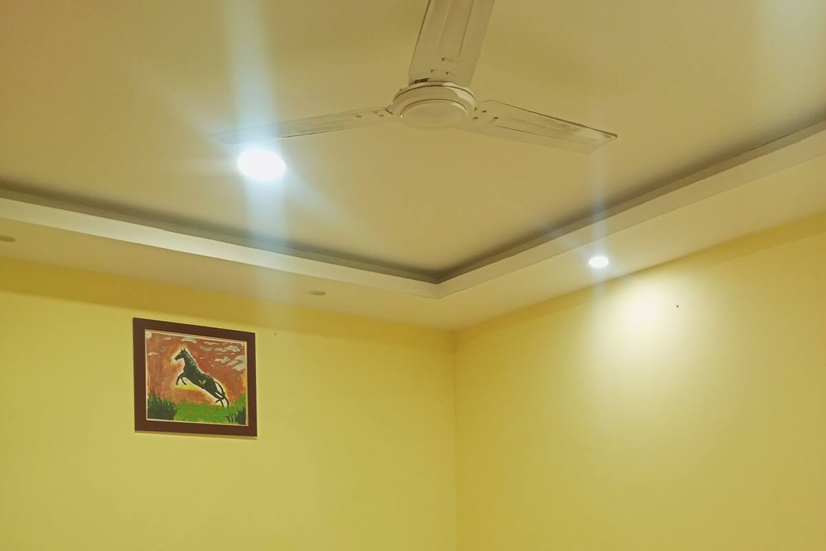A hotel room with a bed, a ceiling fan, and a painting on the wall.